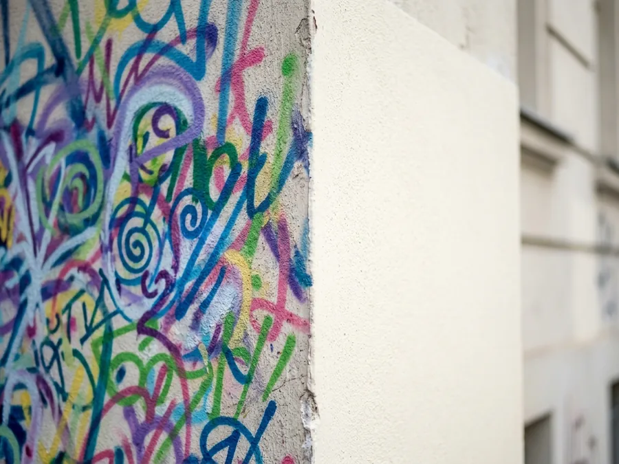 Graffitientfernung an einer Hausfassade: halb gereinigter Putz neben besprühter Fläche