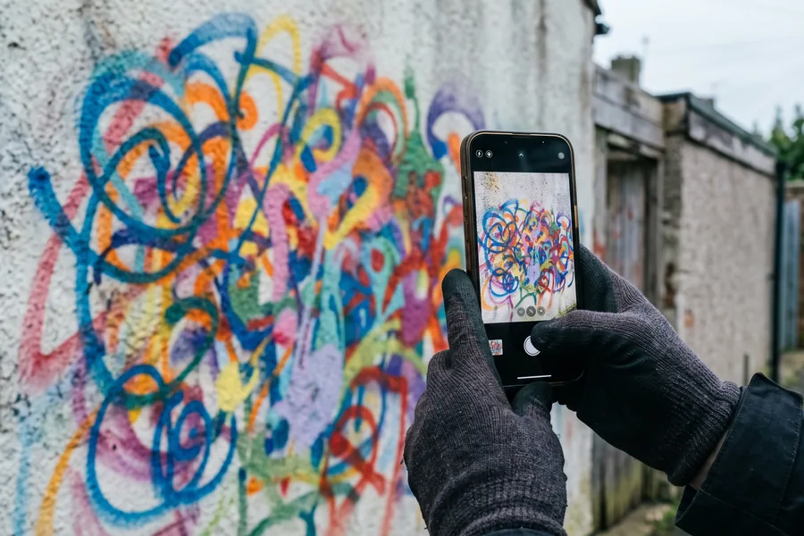 Smartphone fotografiert ein buntes Graffiti an einer Hauswand für die Dokumentation
